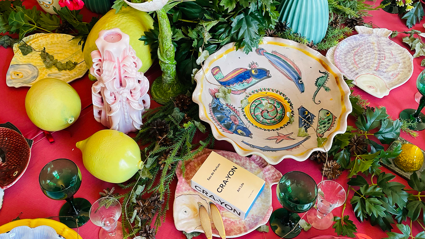 Colorful Italian-inspired table setting with lemons, ceramic plates, greenery, and CRA-YON Art Life perfume box centerpiece.