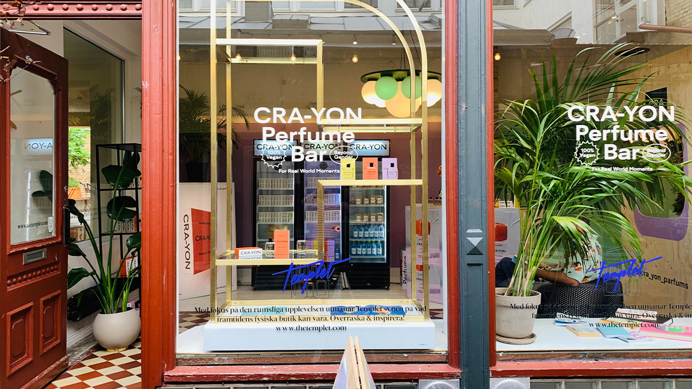 CRA-YON Perfume Bar storefront with colorful perfumes and green plants in a bright city setting.