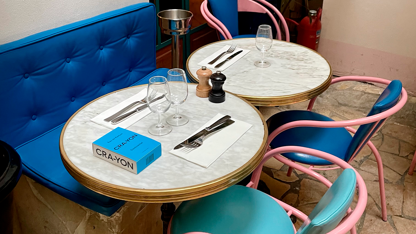CRA-YON Continental perfume box on a stylish café table with colorful chairs and table setting.