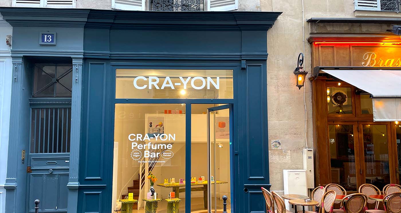 CRA-YON Perfume Bar storefront in Paris with vibrant blue facade next to a cozy French café terrace.