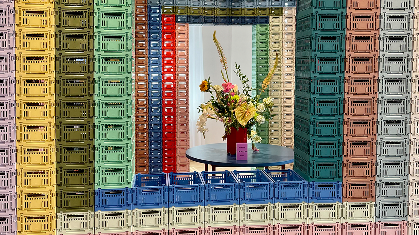 A burst of color: Crate installation framing a floral bouquet with CRA-YON perfume on a blue table