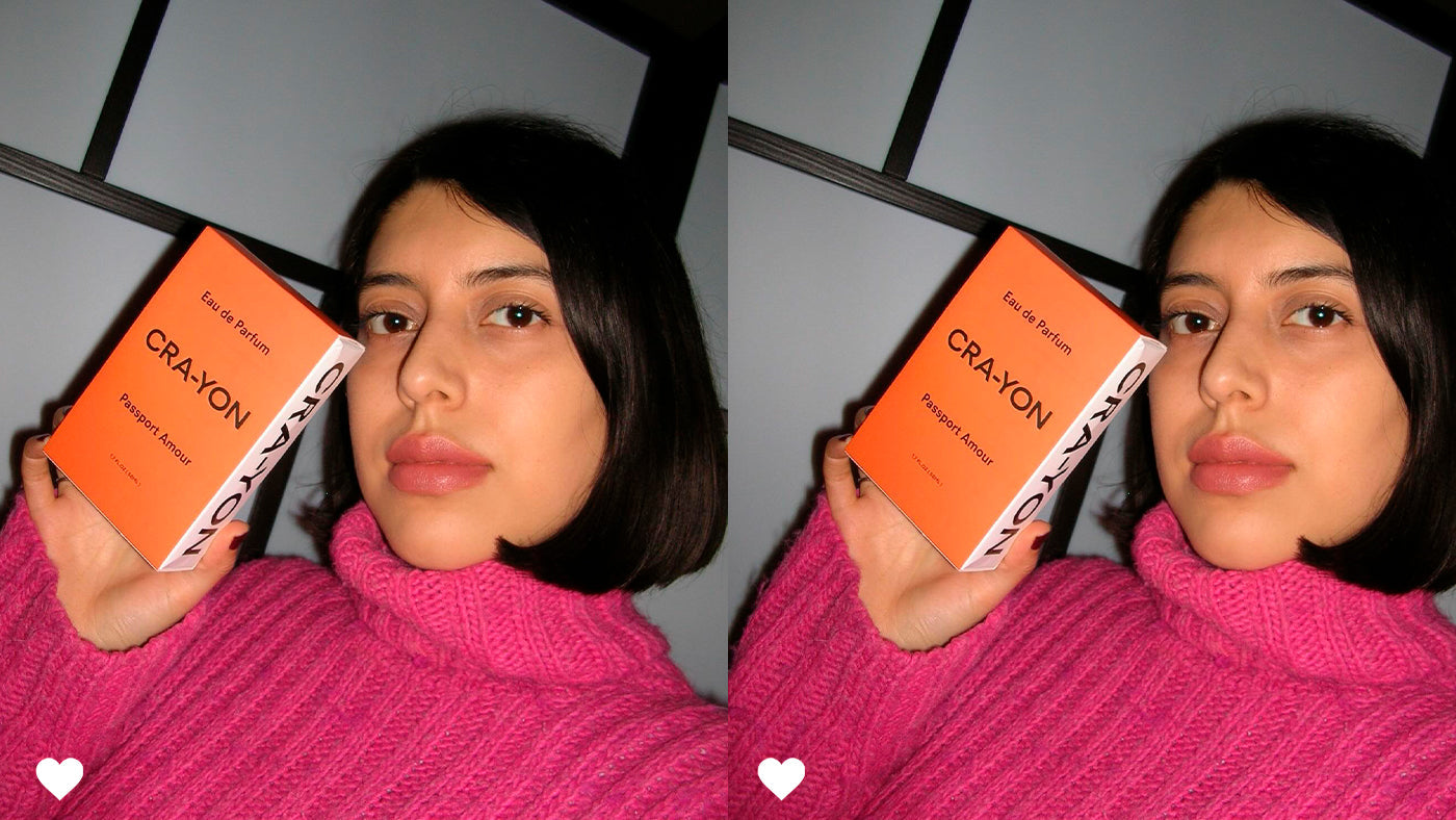 Person in bright pink sweater holding CRA-YON 'Passport Amour' perfume box, mirrored side by side