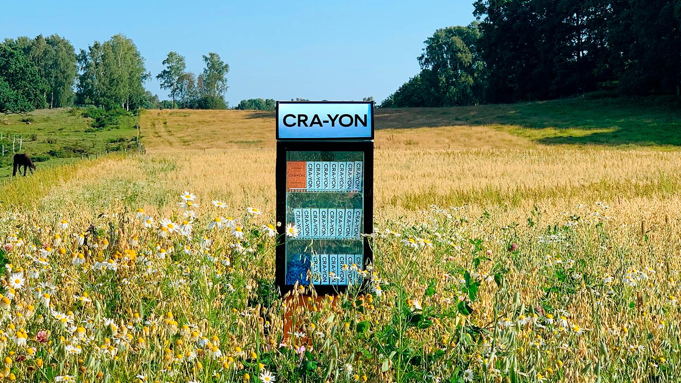CRA-YON branded perfume fridge standing in a colorful wildflower field on a sunny summer day.