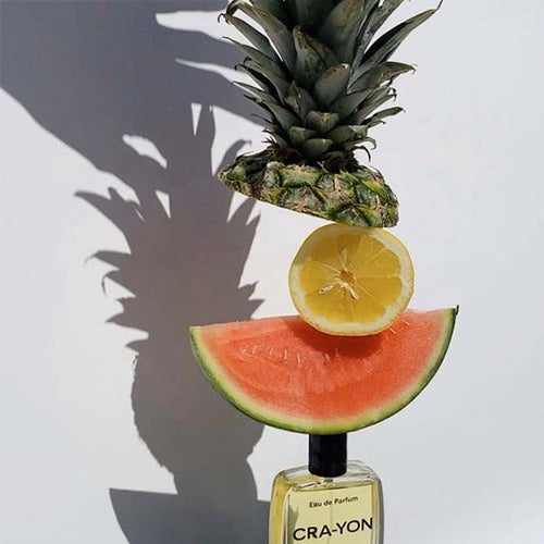 CRA-YON perfume bottle topped with stacked pineapple, lemon, and watermelon slices against white background