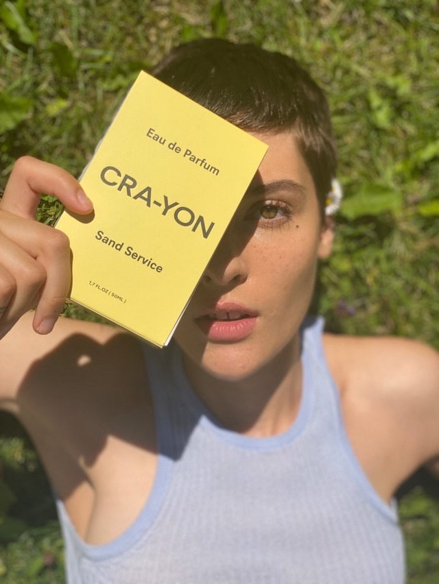 Girl laying on grass with Sand Service yellow packaging in front of her face