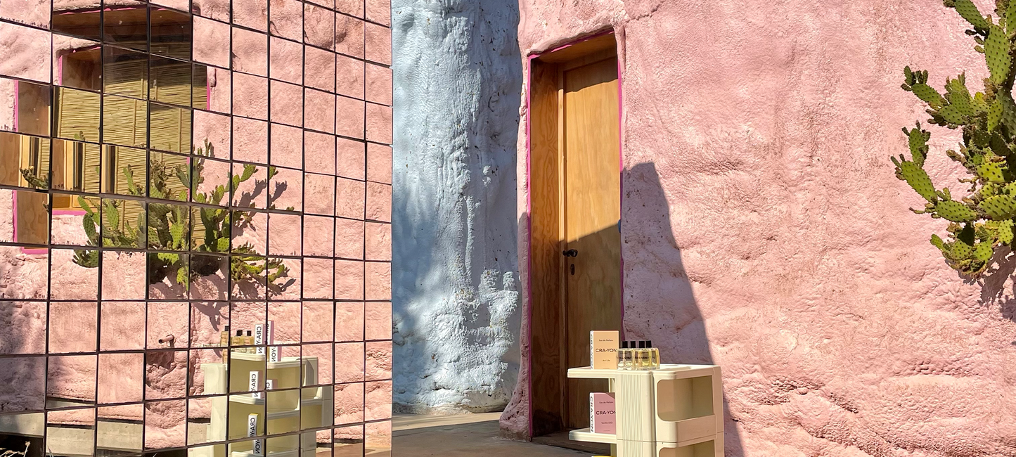 CRA-YON perfumes displayed against pink stucco wall with cactus and mirror reflections in a sunlit desert-inspired setting