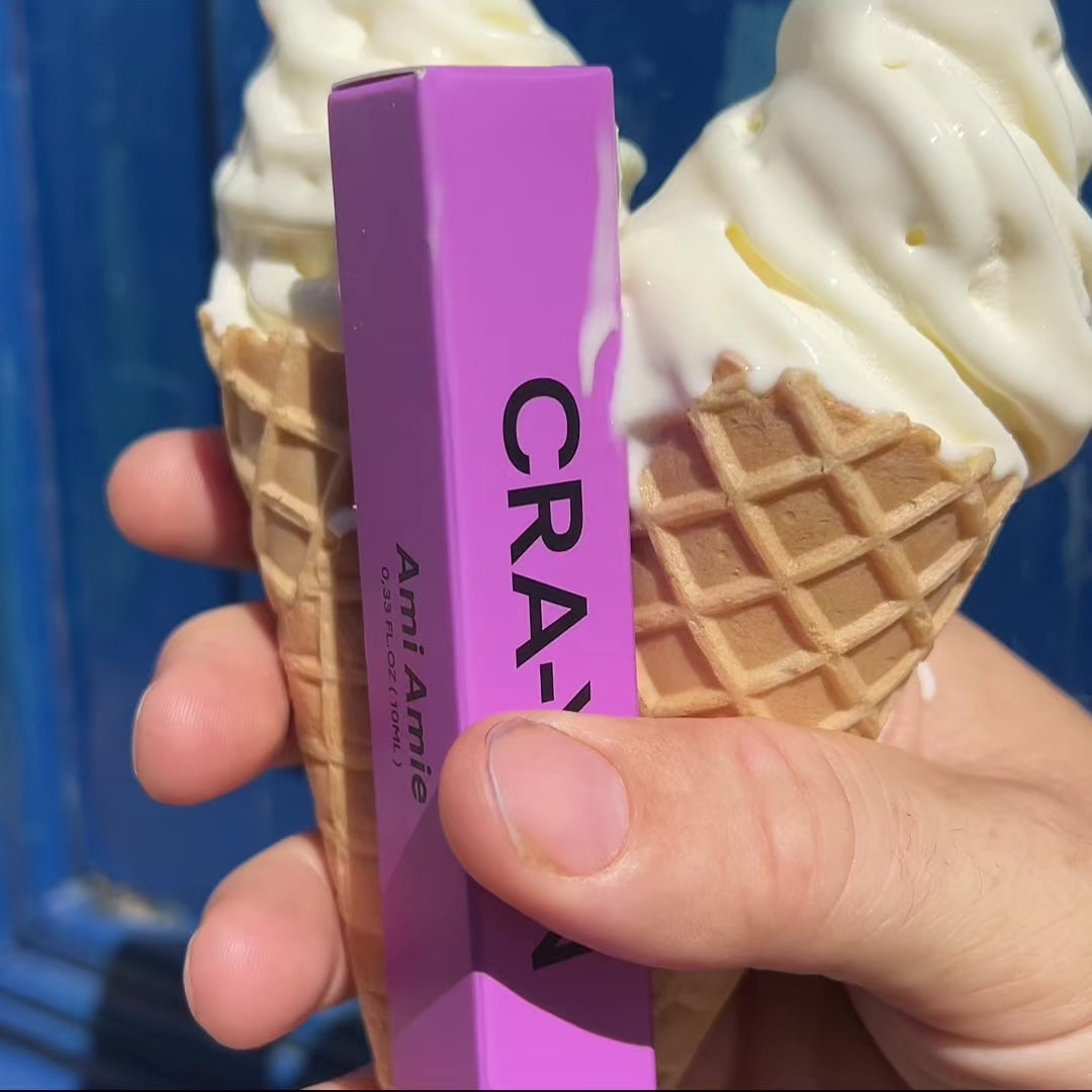 Hand holding two vanilla ice cream cones and a purple CRA-YON Ami Amie perfume box.
