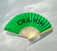 Bright green handheld fan with 'CRA-YON' text, lying open on a light surface with soft shadows